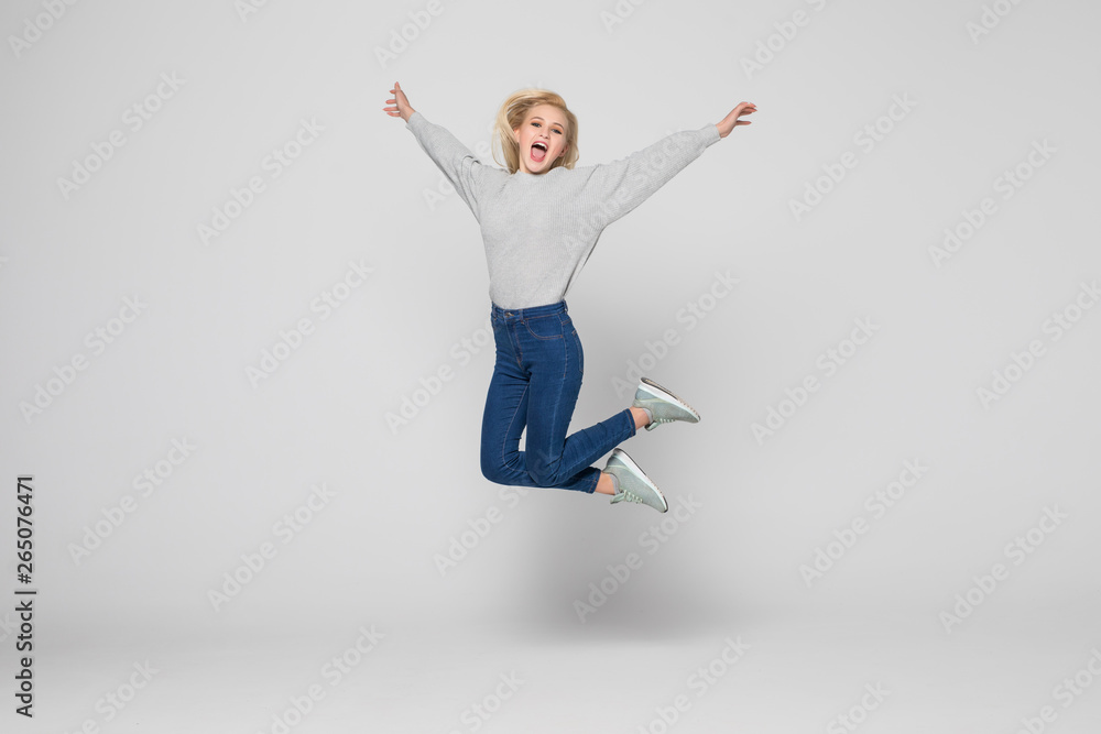Fototapeta premium Full length portrait of a cheerful young woman jumping and celebrating over gray background