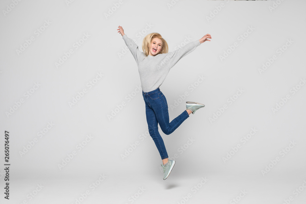 Fototapeta premium happiness, freedom, movement and people concept. Smiling young woman jumping in air isolated on gray background
