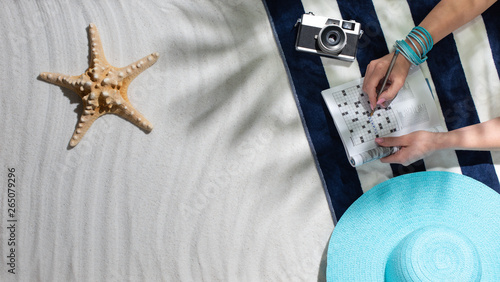 Fototapeta Naklejka Na Ścianę i Meble -  Woman relaxing on the beach and solving crosswords