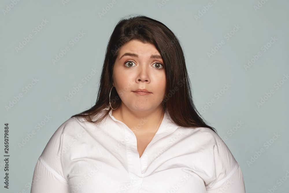 Astonishment, surprise, shock and amazement. Attractive emotional young brunette female employee with excess weight having scared shocked facial expression while being reprimanded by her angry boss Astonishment, surprise, shock and amazement. Attractive emotional young brunette female employee with excess weight having scared shocked facial expression while being reprimanded by her angry boss