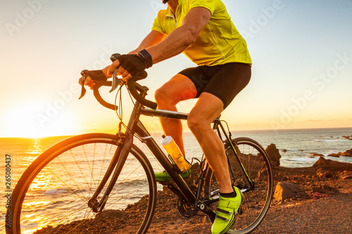 Fototapeta Naklejka Na Ścianę i Meble -  Bike race at sunset road biking cyclist riding bicycle outdoor with sun flare closeup of legs and yellow cycle shoes.
