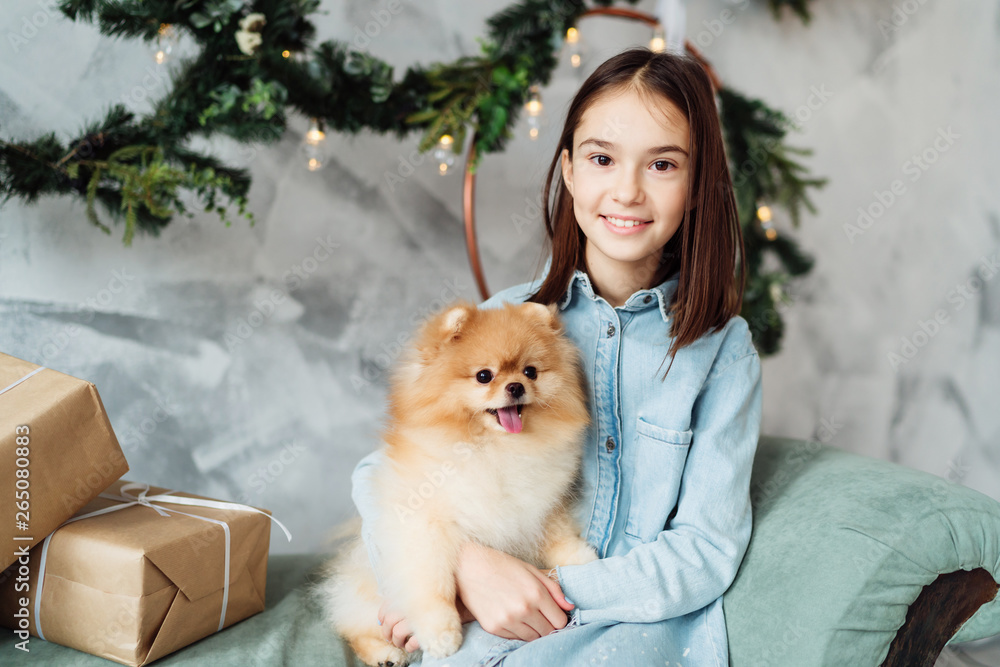 Child girl is holding puppy on her hands on the sofa in her decorated bedroom