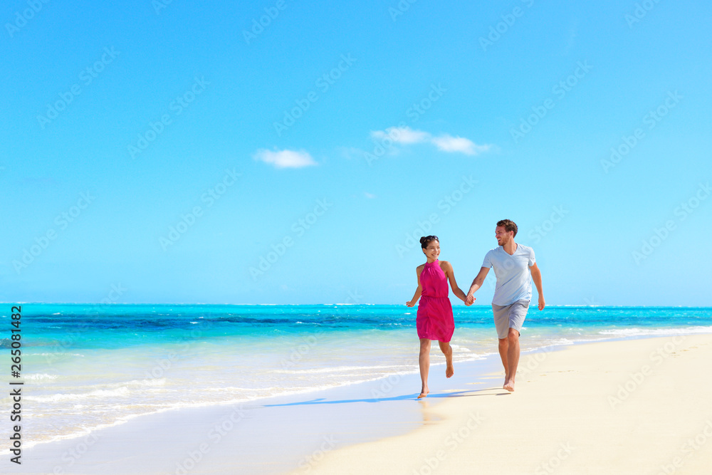 Beach vacation honeymoon paradise travel destination - Young couple in love walking holding hands in idyllic holiday background.