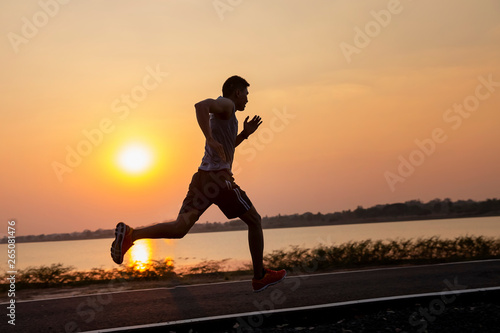 Fototapeta Naklejka Na Ścianę i Meble -  Handsome young man running on a rural road at sunset in summer field. silhouette, running sportsman in the sun, toning. Lifestyle sports background .
