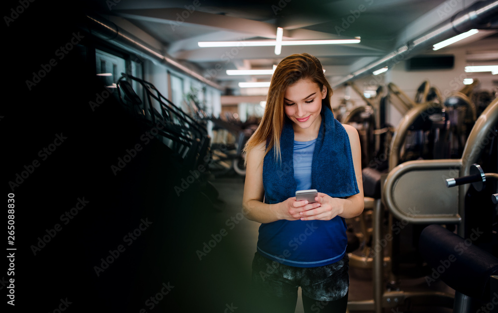 A portrait of young girl or woman with smartphone in a gym. A portrait of young girl or woman with smartphone in a gym.