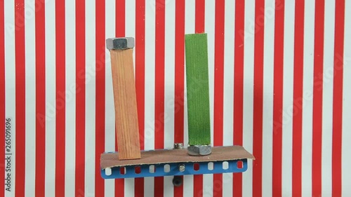 Two alike wood blocks with a metal at one end paced on a board that tgradually tilts, one by one they fall. The background lines are vertical reference,  photo