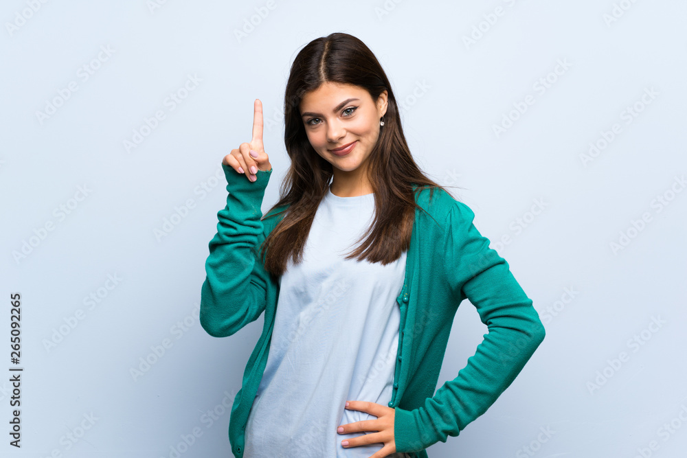 Teenager girl over blue wall showing and lifting a finger in sign of the best Teenager girl over blue wall showing and lifting a finger in sign of the best