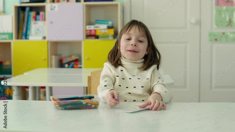 Lonely girl in kindergarten. Child, girl 5-6 years old, draws, sitting at the table. A blonde girl wearing a white knitted sweater. She draws with pencils. Lonely girl in kindergarten. Child, girl 5-6 years old, draws, sitting at the table. A blonde girl wearing a white knitted sweater. She draws with pencils.