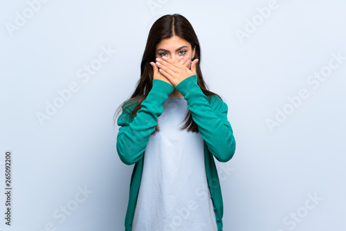 Teenager girl over blue wall covering mouth with hands © luismolinero