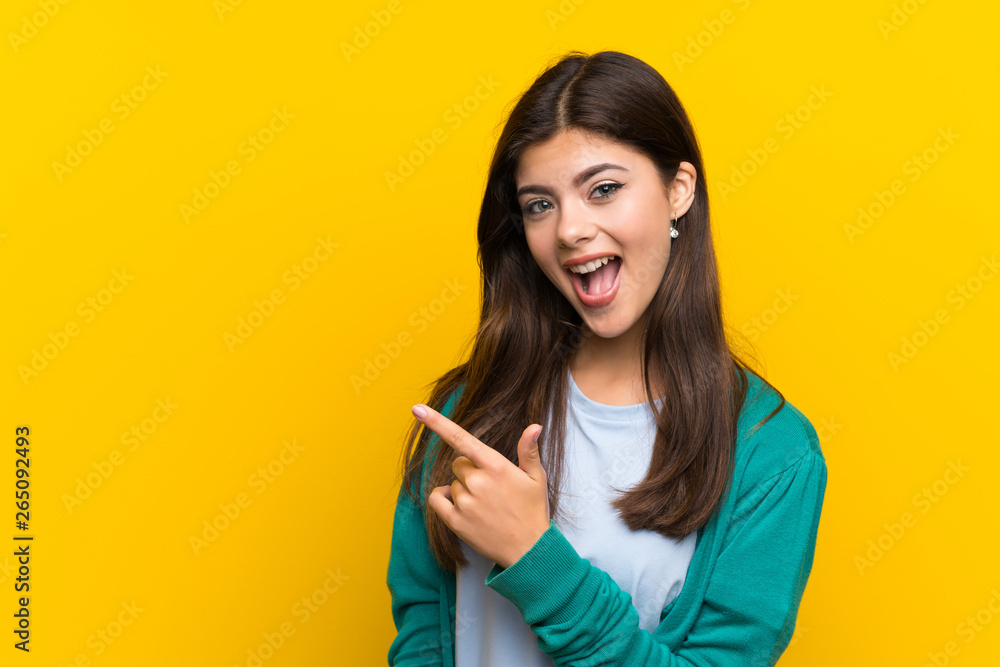 Teenager girl over yellow wall pointing finger to the side Teenager girl over yellow wall pointing finger to the side