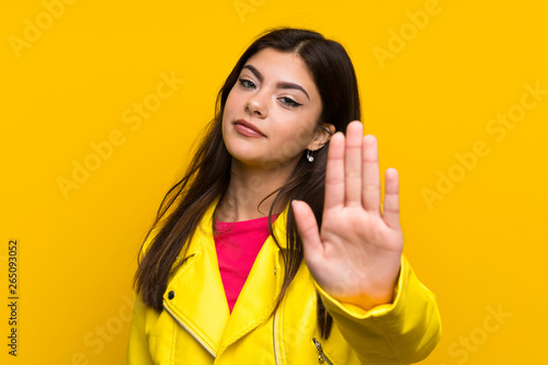 Teenager girl over yellow wall making stop gesture with her hand
