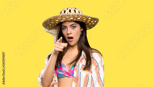 Teenager girl on summer vacation surprised and pointing front over isolated yellow background