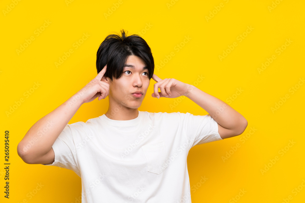 Asian man over isolated yellow wall having doubts and thinking Asian man over isolated yellow wall having doubts and thinking