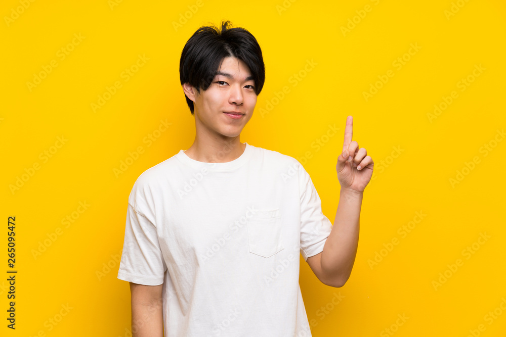 Asian man over isolated yellow wall showing and lifting a finger in sign of the best Asian man over isolated yellow wall showing and lifting a finger in sign of the best