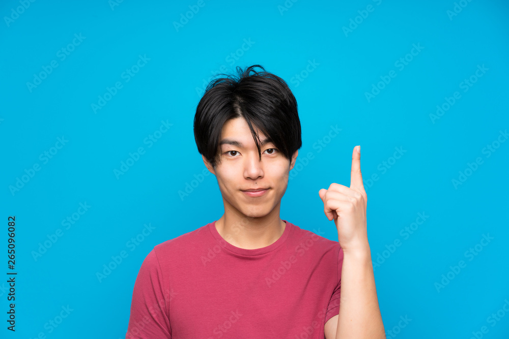 Asian man with red shirt over isolated blue wall pointing with the index finger a great idea Asian man with red shirt over isolated blue wall pointing with the index finger a great idea