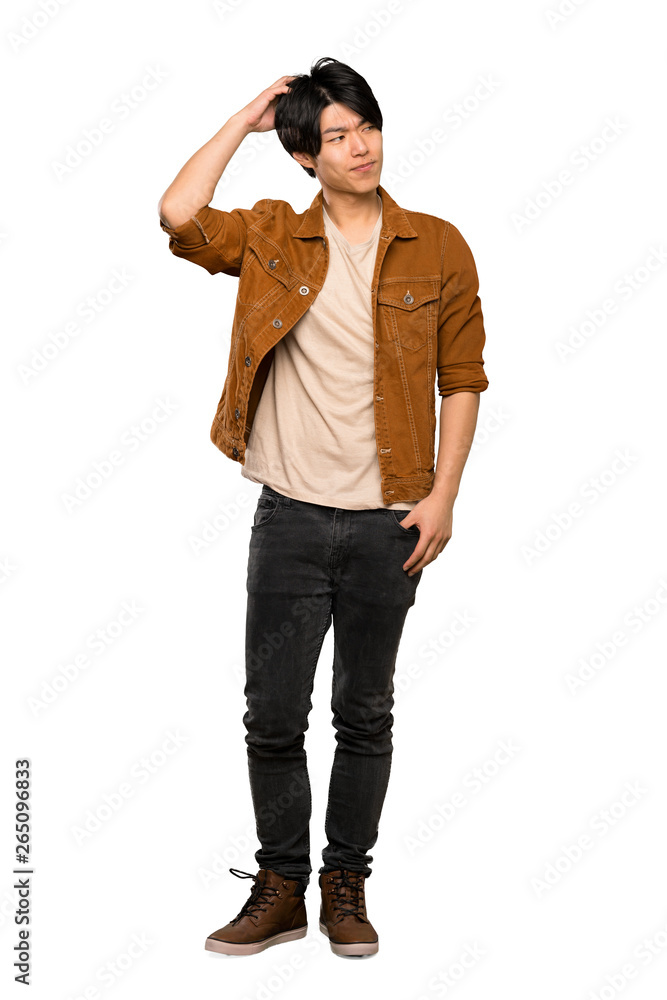 A full-length shot of a Asian man with brown jacket having doubts while scratching head over isolated white background A full-length shot of a Asian man with brown jacket having doubts while scratching head over isolated white background