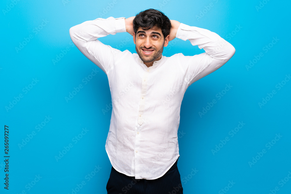 Young man over isolated blue wall takes hands on head because has migraine Young man over isolated blue wall takes hands on head because has migraine
