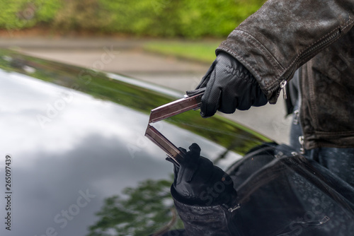 A person scratches the bonnet of a car with a blade