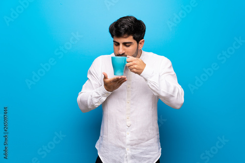 Young man over isolated blue wall holding a hot cup of coffee