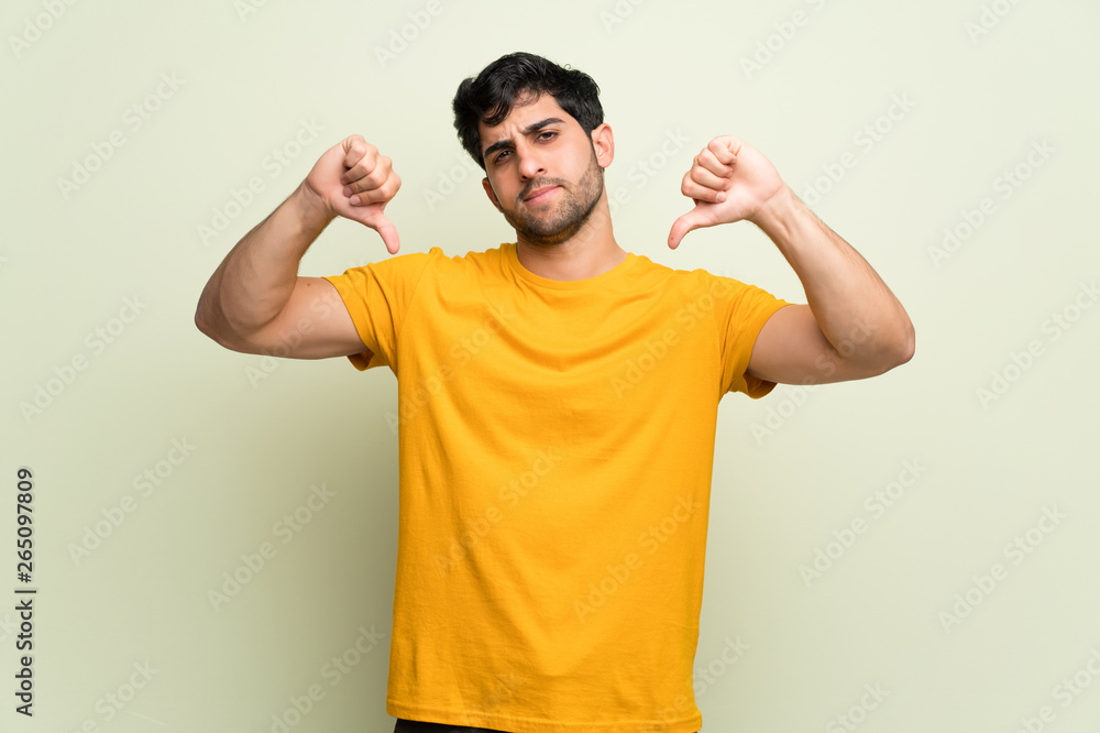Young man over pink wall showing thumb down with both hands Young man over pink wall showing thumb down with both hands