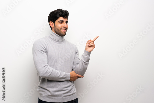 Young man over isolated white wall pointing finger to the side