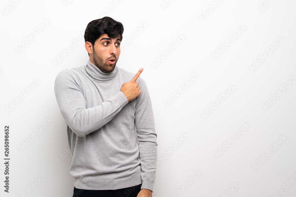 Young man over isolated white wall surprised and pointing side Young man over isolated white wall surprised and pointing side