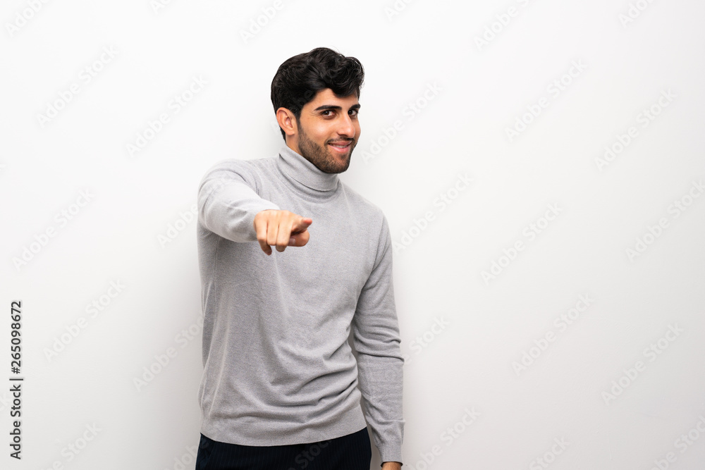 Young man over isolated white wall points finger at you with a confident expression Young man over isolated white wall points finger at you with a confident expression