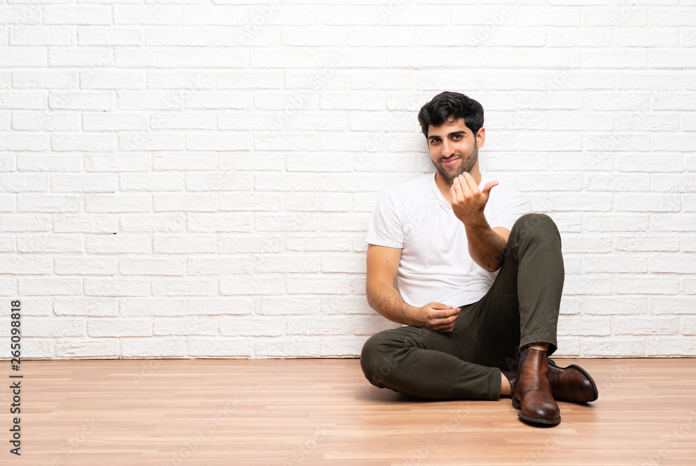 Young man sitting on the floor inviting to come with hand. Happy that you came Young man sitting on the floor inviting to come with hand. Happy that you came