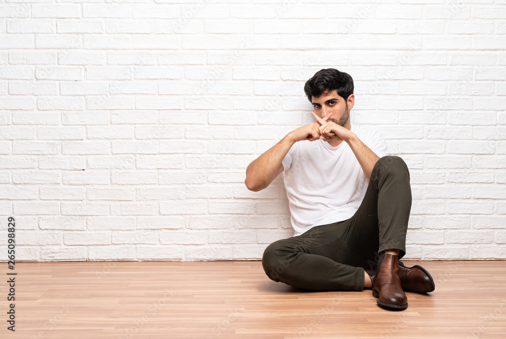 Young man sitting on the floor showing a sign of silence gesture Young man sitting on the floor showing a sign of silence gesture