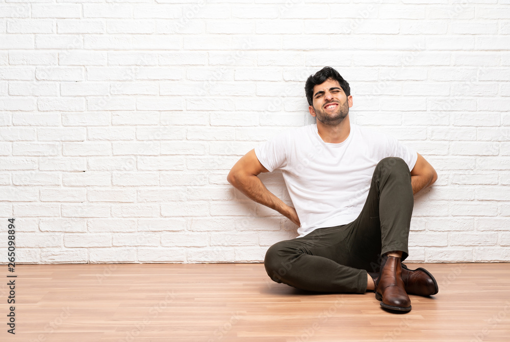 Young man sitting on the floor suffering from backache for having made an effort Young man sitting on the floor suffering from backache for having made an effort