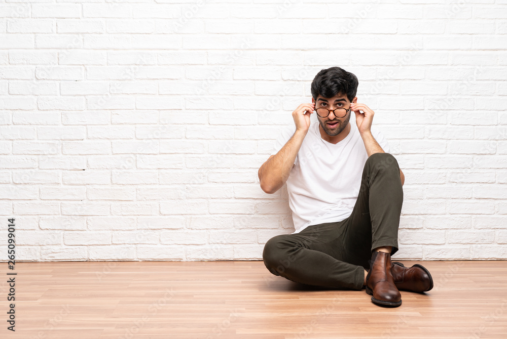 Young man sitting on the floor with glasses and surprised Young man sitting on the floor with glasses and surprised