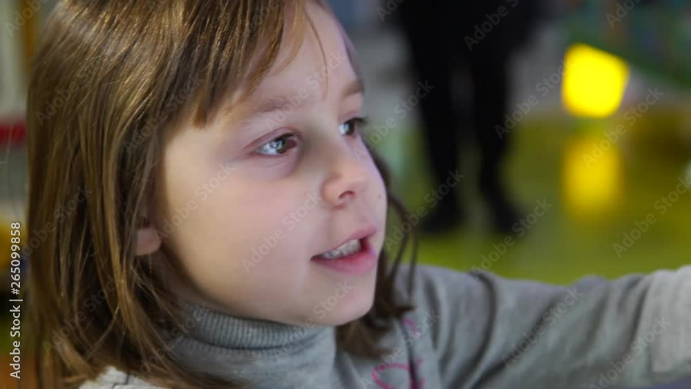 The girl solves the problem on the electronic device. A child at a children's playground in a shopping center. The girl solves the problem on the electronic device. A child at a children's playground in a shopping center.