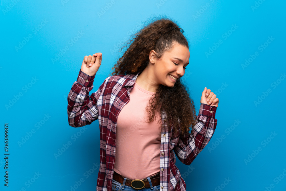 Teenager girl over blue wall enjoy dancing while listening to music at a party Teenager girl over blue wall enjoy dancing while listening to music at a party