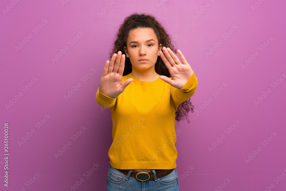 Teenager girl over purple wall making stop gesture and disappointed