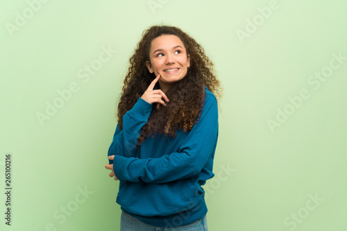 Teenager girl over green wall thinking an idea while looking up