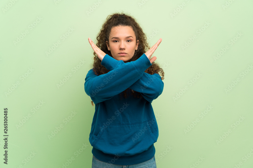 Teenager girl over green wall making NO gesture Teenager girl over green wall making NO gesture