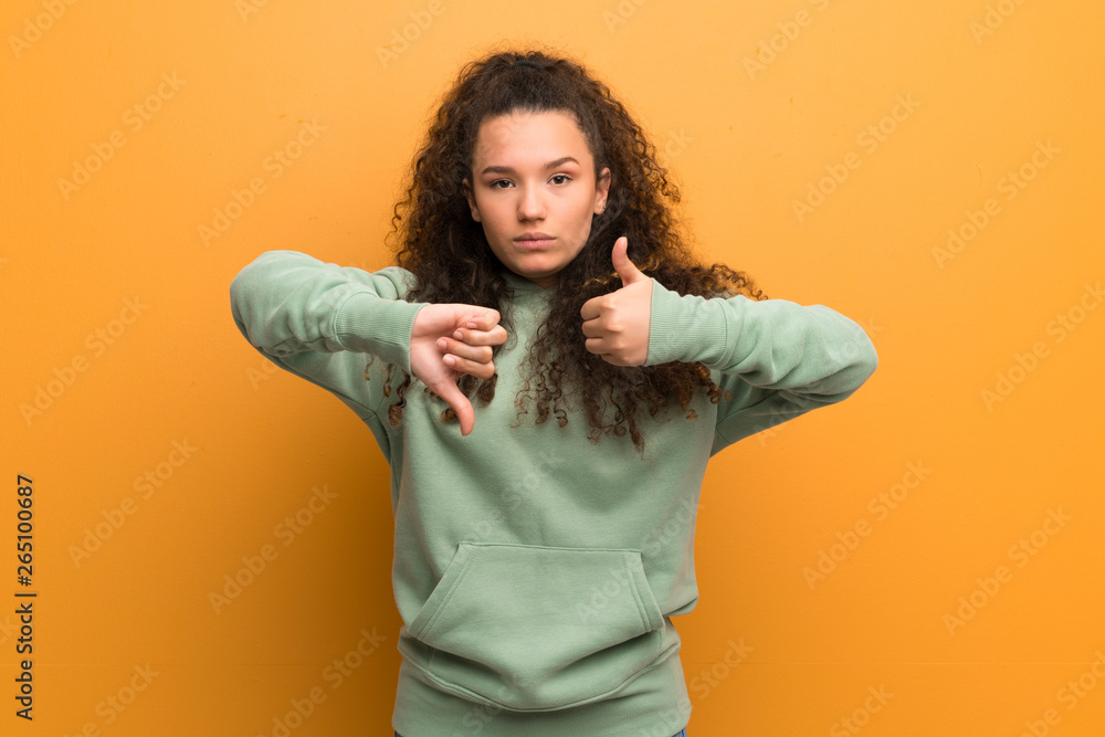 Teenager girl over ocher wall making good-bad sign. Undecided between yes or not Teenager girl over ocher wall making good-bad sign. Undecided between yes or not
