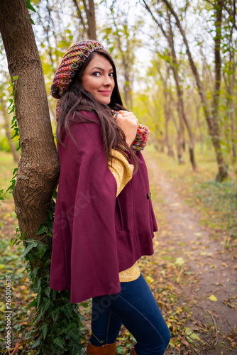 Beautiful girl smiling at the camera, in stylish autumn fashion clothes, in park scenery with trees and leaves. Gorgeous romantic young woman outdoors. Full length shot, retouched, vibrant colors
