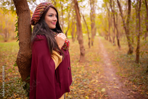 Beautiful girl in stylish autumn fashion clothes, in park scenery with trees and leaves. Gorgeous romantic young woman outdoors. American plan shot in warm natural light, retouched, vibrant colors