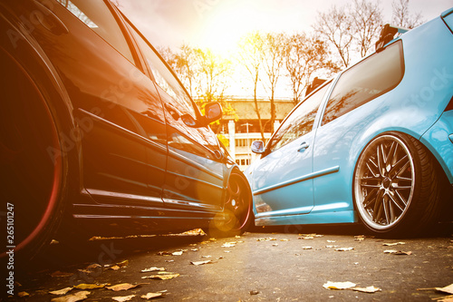 Two modified low cars in brown and light blue color. Stance custom cars with a forged polished wheels parked on a street at sunny day. Tuned automobiles