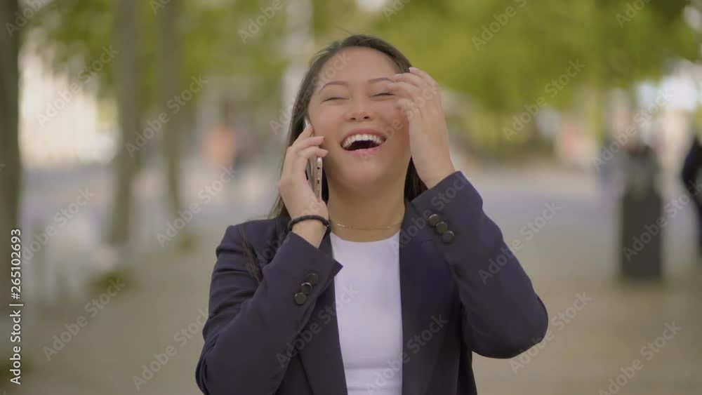 Excited young woman talking by cell phone outdoor. Beautiful shocked girl walking, shaking fist and laughing during pleasant phone talk on street. Good news concept Excited young woman talking by cell phone outdoor. Beautiful shocked girl walking, shaking fist and laughing during pleasant phone talk on street. Good news concept