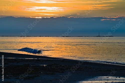 romantic sunset over the sea with a few waves and soft orange light on a lonely beach, cloudy sky
