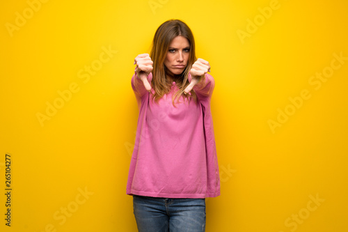 Woman with pink sweater over yellow wall showing thumb down