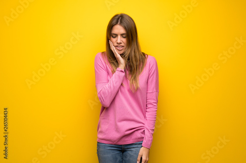 Woman with pink sweater over yellow wall with toothache