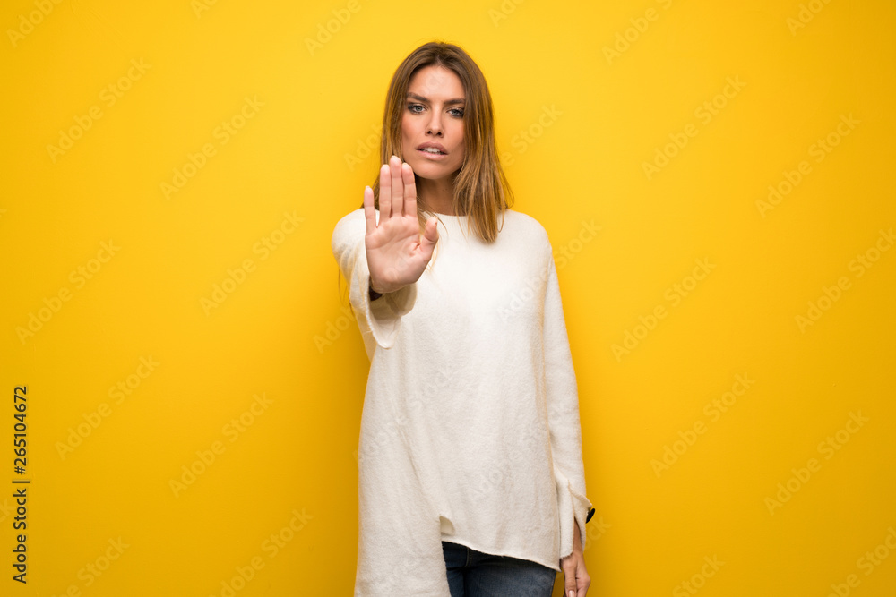Blonde woman over yellow wall making stop gesture denying a situation that thinks wrong Blonde woman over yellow wall making stop gesture denying a situation that thinks wrong