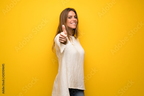Blonde woman over yellow wall giving a thumbs up gesture because something good has happened © luismolinero