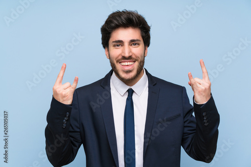 Businessman over isolated blue wall making rock gesture