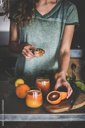 Young female making freshly squeezed blood orange juice or smoothie near concrete kitchen counter. Healthy lifestyle, vegan, vegetarian, alkaline diet, spring detox concept