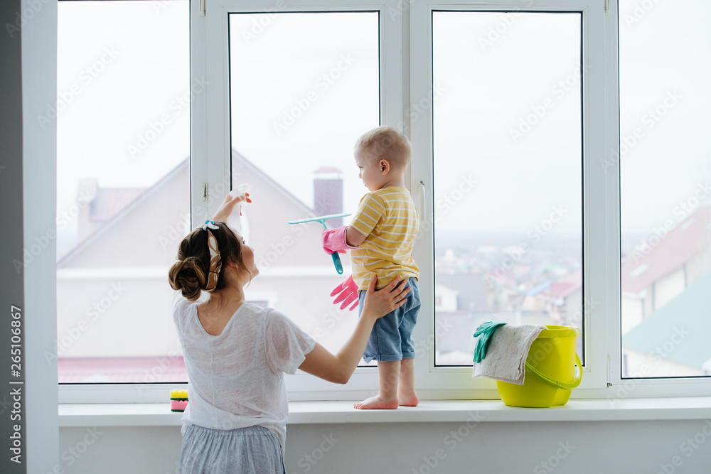 Funny little blond toddler boy is cleaning plastic window door with scrubber - obrazy, fototapety, plakaty 