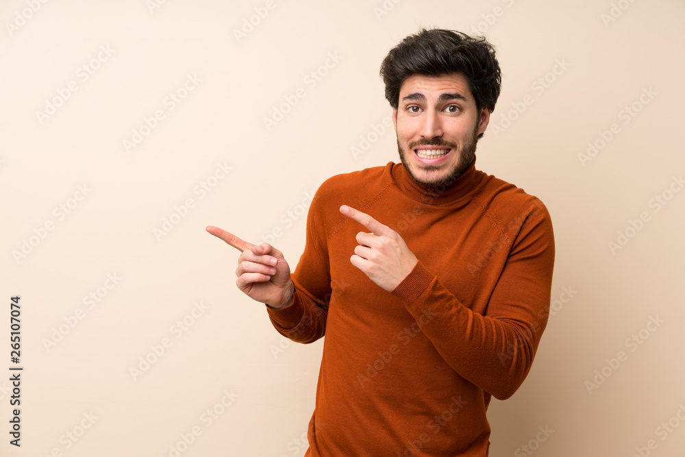 Handsome over isolated wall frightened and pointing to the side Handsome over isolated wall frightened and pointing to the side